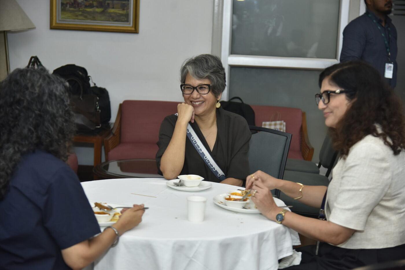 Grey-haired woman in black laughing with her hand on her chin over lunch