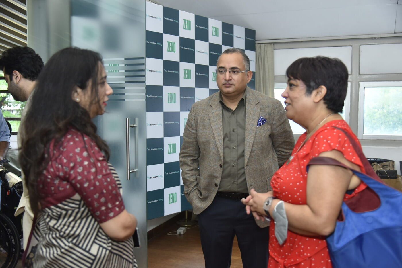 Man in a brown check blazer between two women in front of the ZENO backdrop