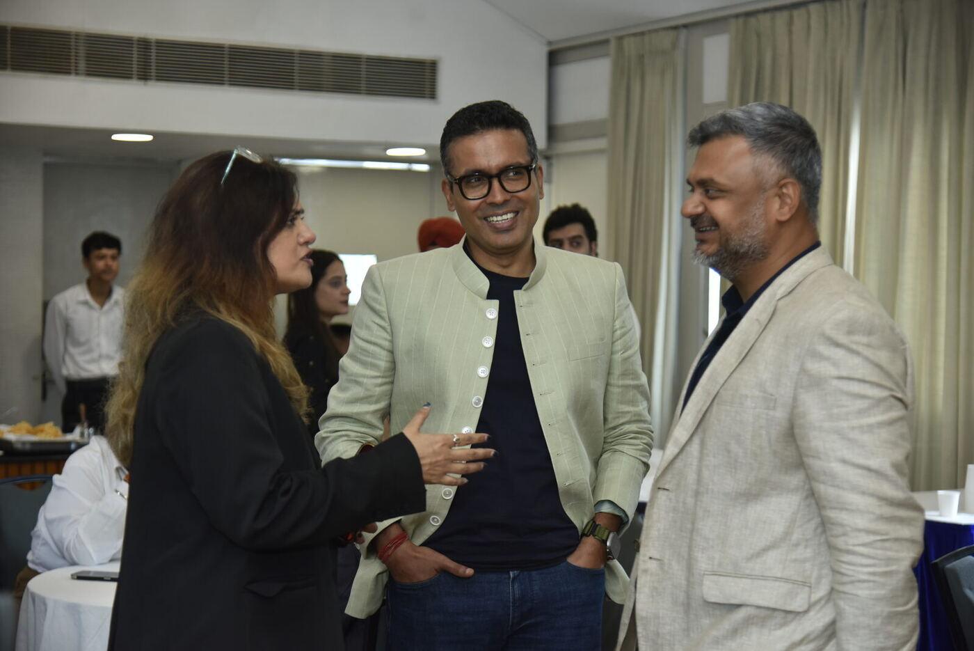 Man in a pale green nehru jacket laughing with a woman in black and a man in beige linen