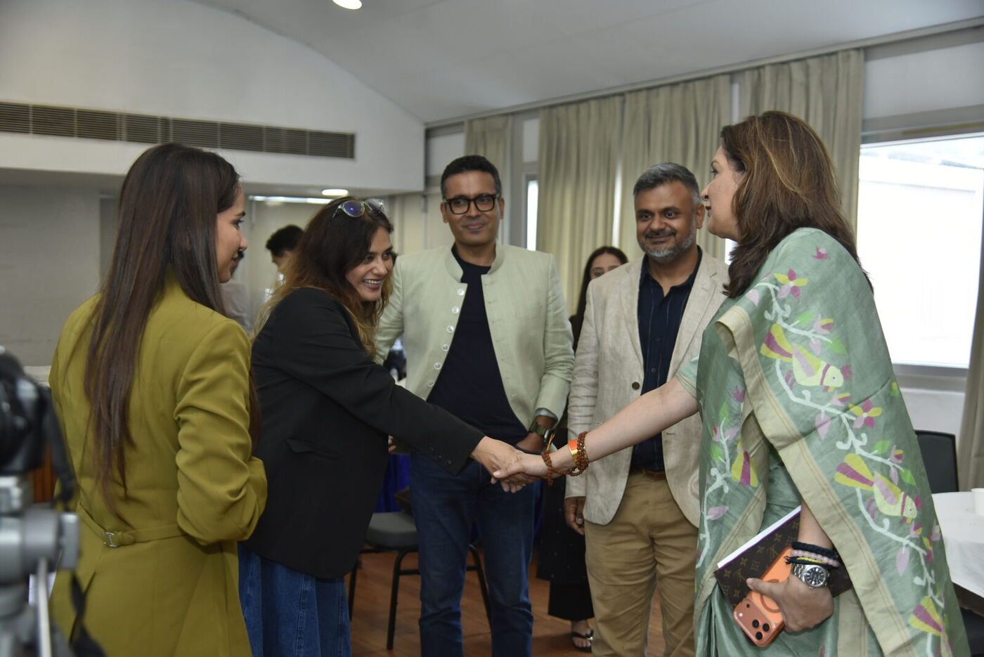 Handshake greeting as the guest in the green Jamdani saree arrives, four others around