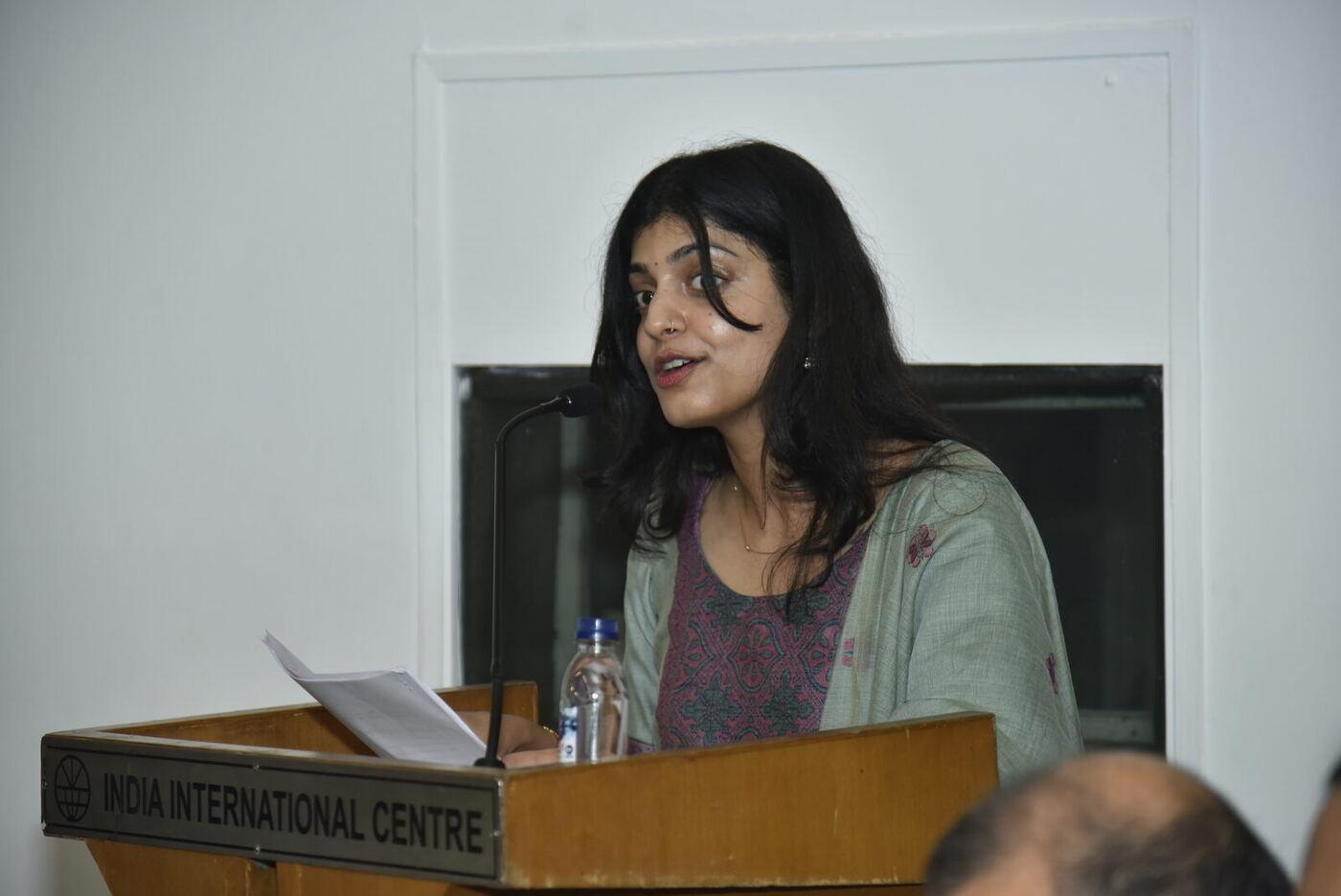 Young host in a mint dupatta mid-sentence at the India International Centre podium