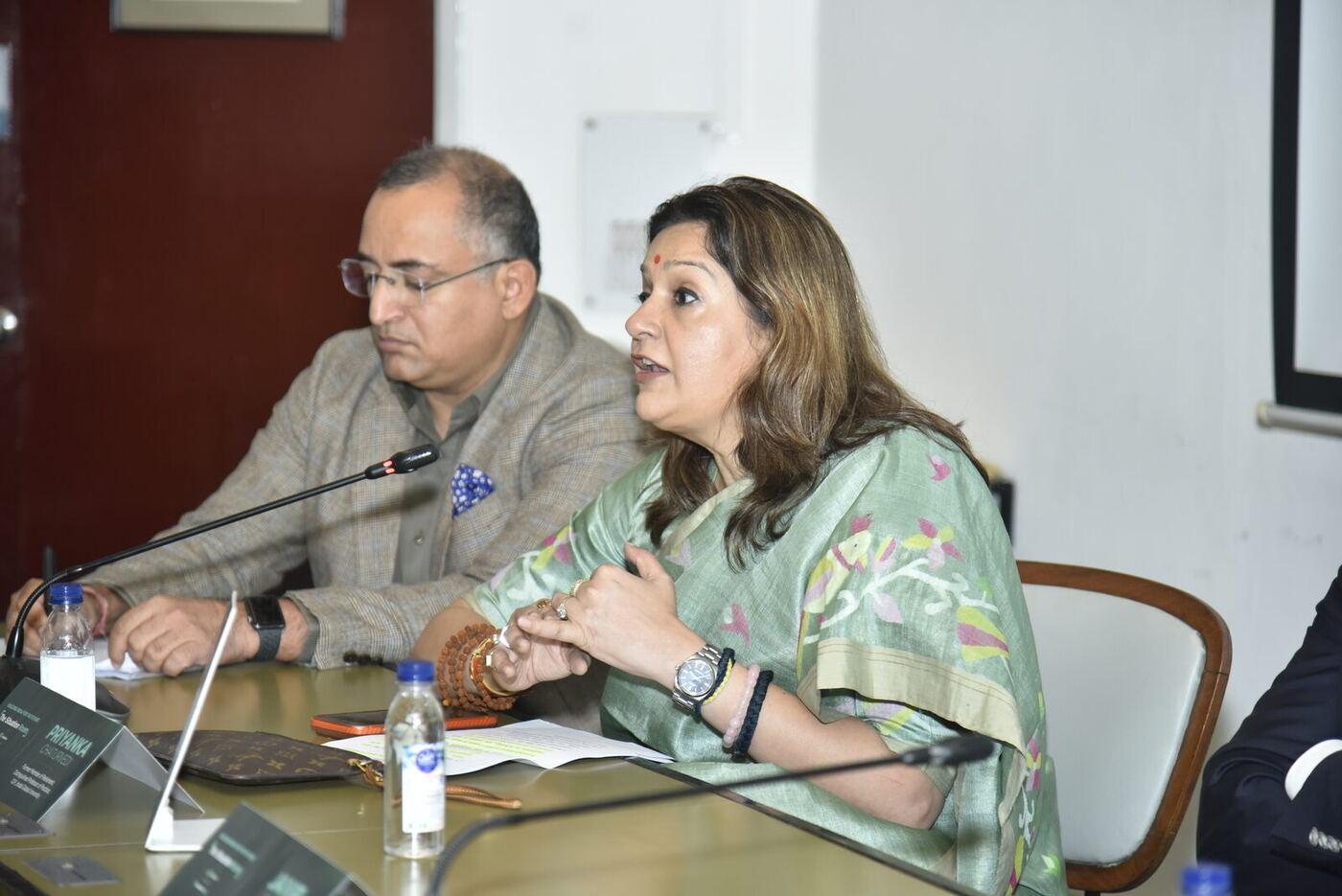 Two-shot: Priyanka Chaturvedi gesturing as she speaks, moderator listening beside her