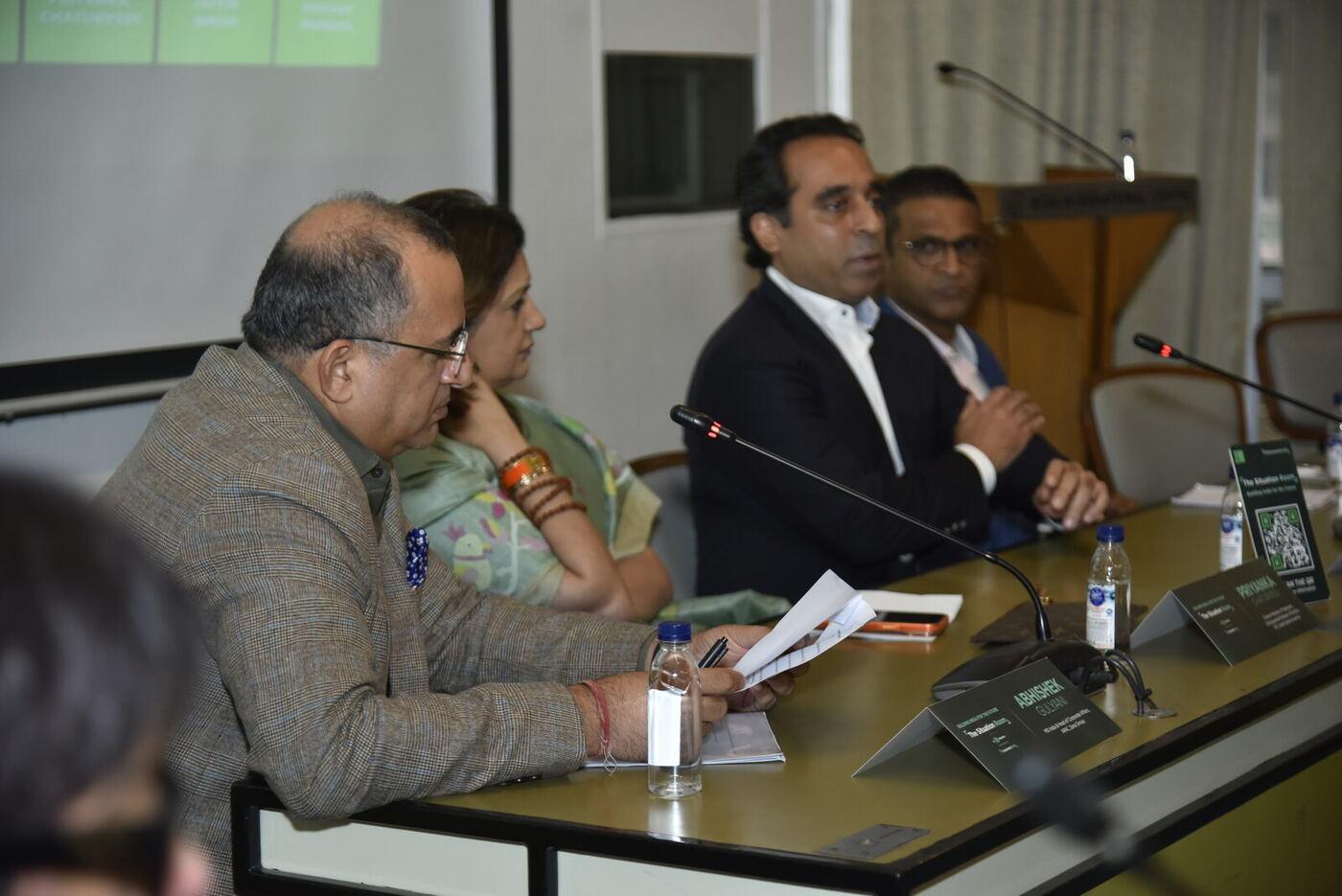 Moderator in tweed reading his notes in the foreground, three panellists behind him