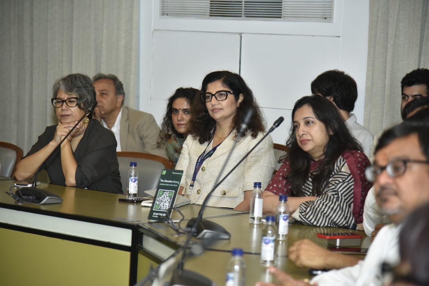Three women listening intently - grey hair in black, cream blazer with lanyard, maroon stripes