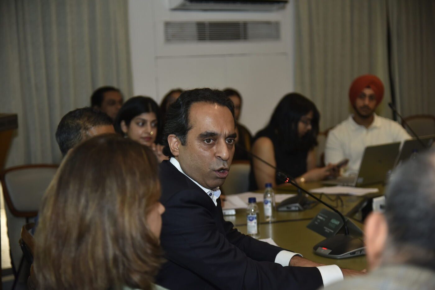 Jaivir Singh turned toward camera mid-answer, turbaned attendee at a laptop behind