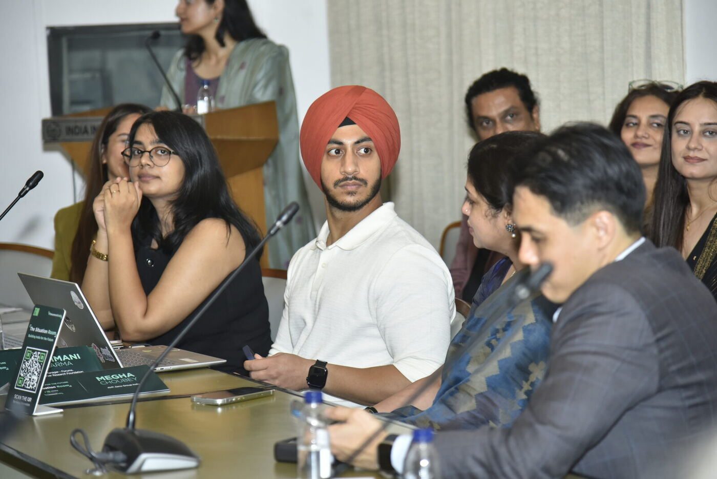 Young man in a red turban listening, two women working at laptops to his left
