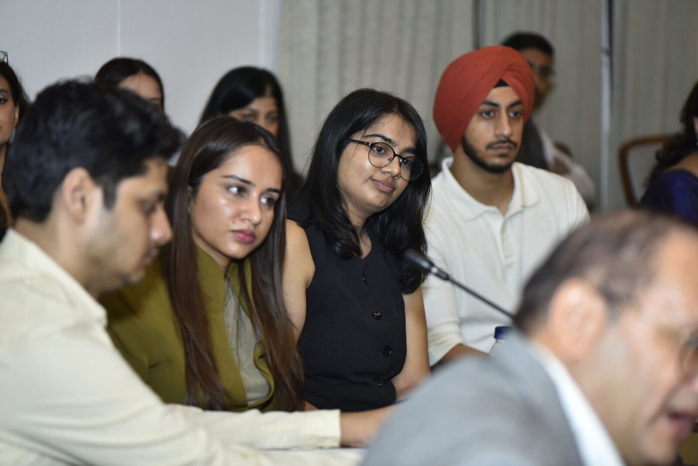 Young woman in black with glasses smiling faintly, turbaned delegate beside her