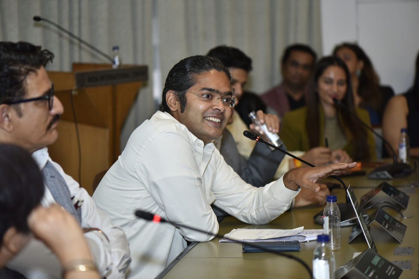 Apurv Kumar Mishra grinning broadly mid-point, hand open over the table
