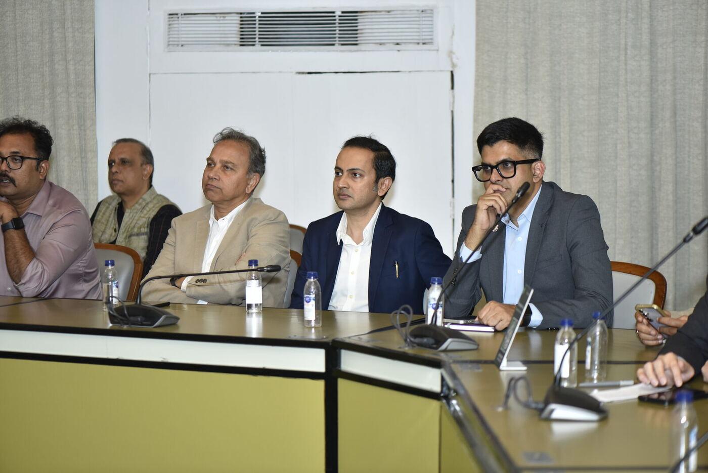 Four men along the delegate table listening, the one at right hand to his chin
