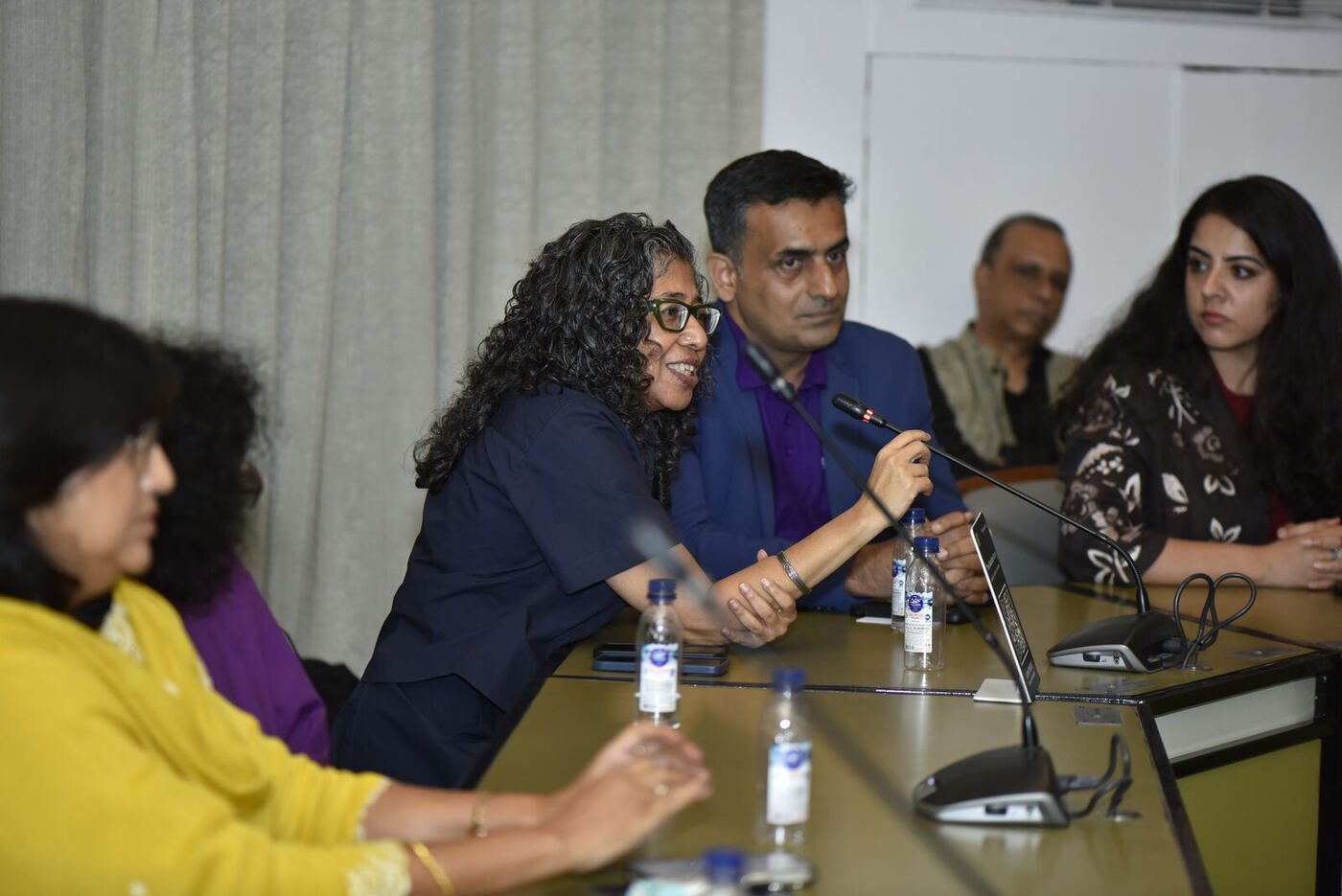 Curly-haired woman in navy leaning into the mic to ask a question